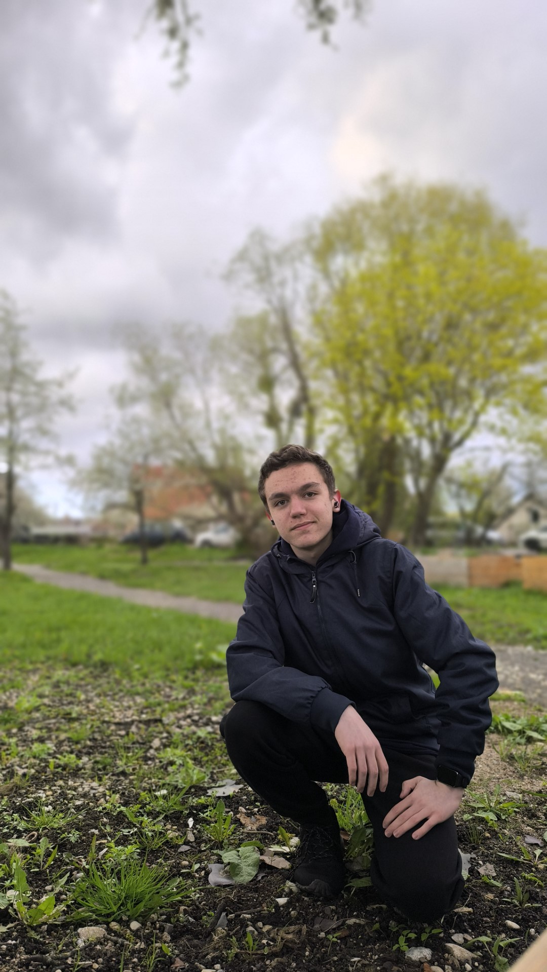 Me crouching down on the ground, a tree is seen in the background and a path is behind me.